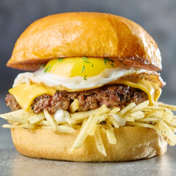 Gutenburg burger with a fried egg, melted cheese, crispy fries, and mayonnaise on a bun.
