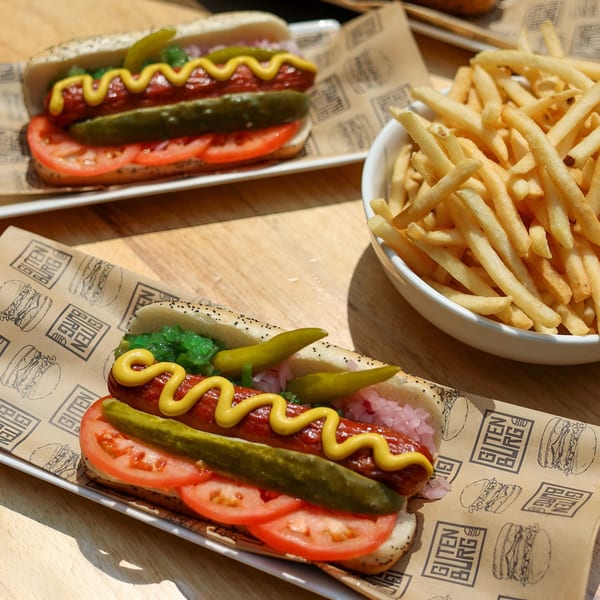 Two Gutenburg hot dogs with mustard, relish, pickles, and tomatoes, served with a side of fries.
