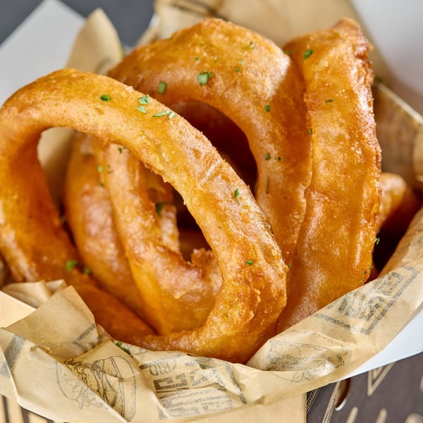 Golden-brown, crispy onion rings with green herbs, served in a paper-lined basket at Gutenburg.