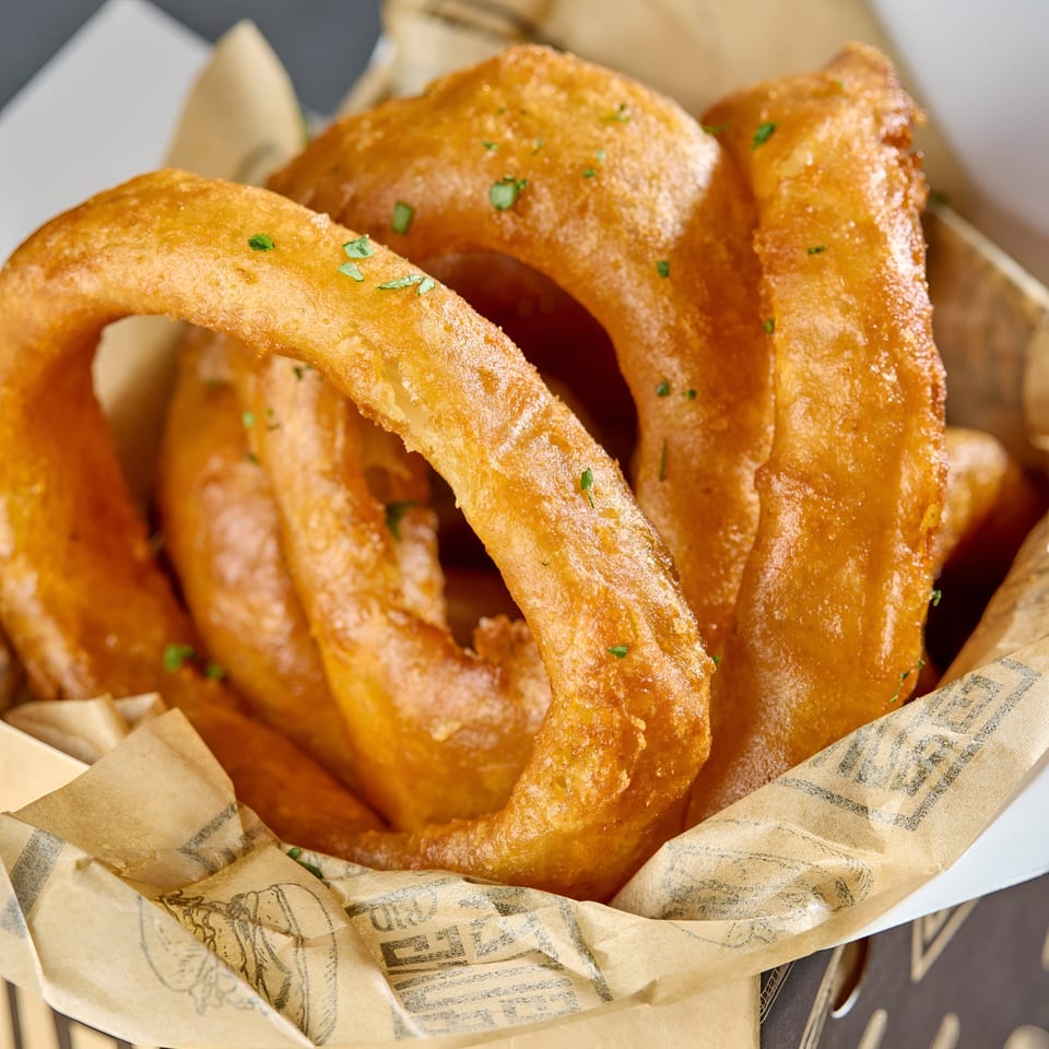 Golden-brown, crispy onion rings with green herbs, served in a paper-lined basket at Gutenburg.