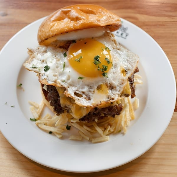 Gutenburg burger with a fried egg, melted cheese, and crispy fries on a white plate.