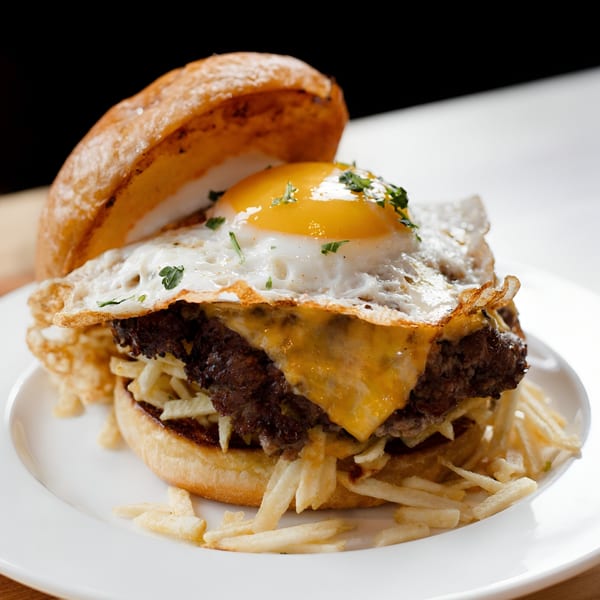 Gutenburg burger with a fried egg, melted cheese, and shoestring fries on a white plate.