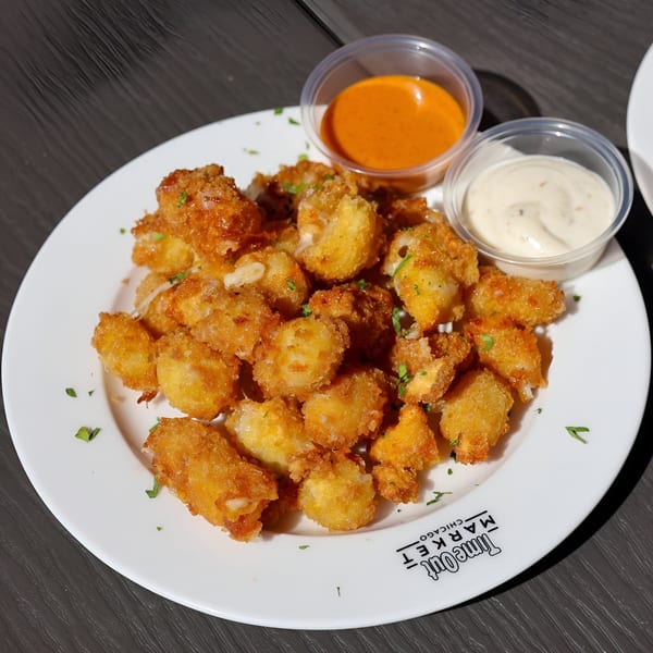 A white plate of golden-brown fried cheese curds with two dipping sauces on a dark table.